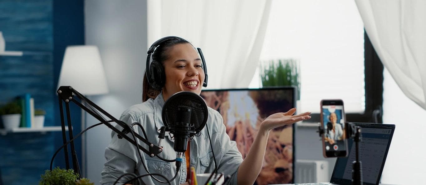 Une jeune influenceuse portant des écouteurs enregistre une vidéo avec un téléphone intelligent pendant qu’elle parle à son public.