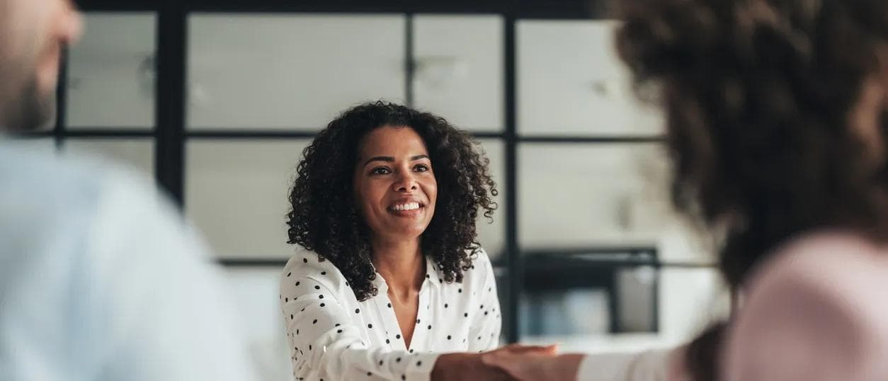 Une femme gestionnaire serre une main au-dessus d’une table, représentant une transaction d’affaires réussie.  